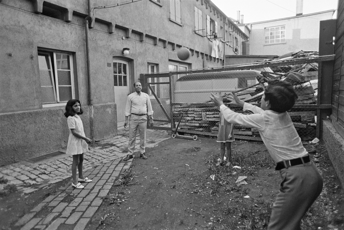 Zu sehen ist ein älteres Ehepaar und einige Kinder, die gemeinsam an einem Tisch sitzen und essen.