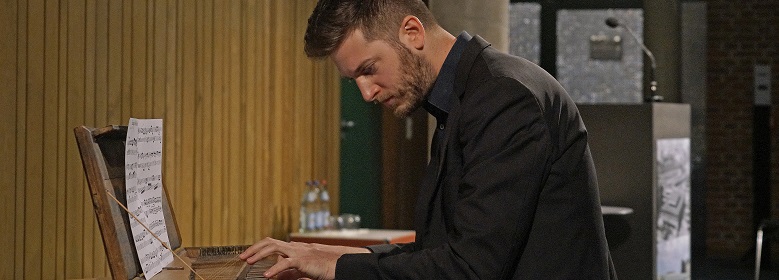 Zu sehen ist ein Mann, der ein schwarzes Hemd trägt und Klavier spielt.