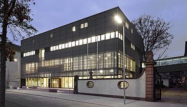 Ausschnitt aus Foto des Neubaus des Generallandesarchivs Karlsruhe am Abend. Die Fenster des Gebäudes sind erleuchtet.