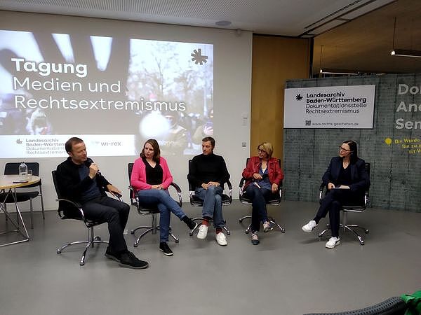 Foto (farbig) der Podiumsdiskussion bei der Tagung 'Medien und Rechtsextremismus'. Die fünf Teilnehmenden sitzen nebeneinander auf Stühlen; von links nach rechts Georg Restle, Ann-Katrin Müller, Holger Stark, Susanne Stiefel und Caroline Walter. Georg Restle hat ein Mikrofon in der Hand.