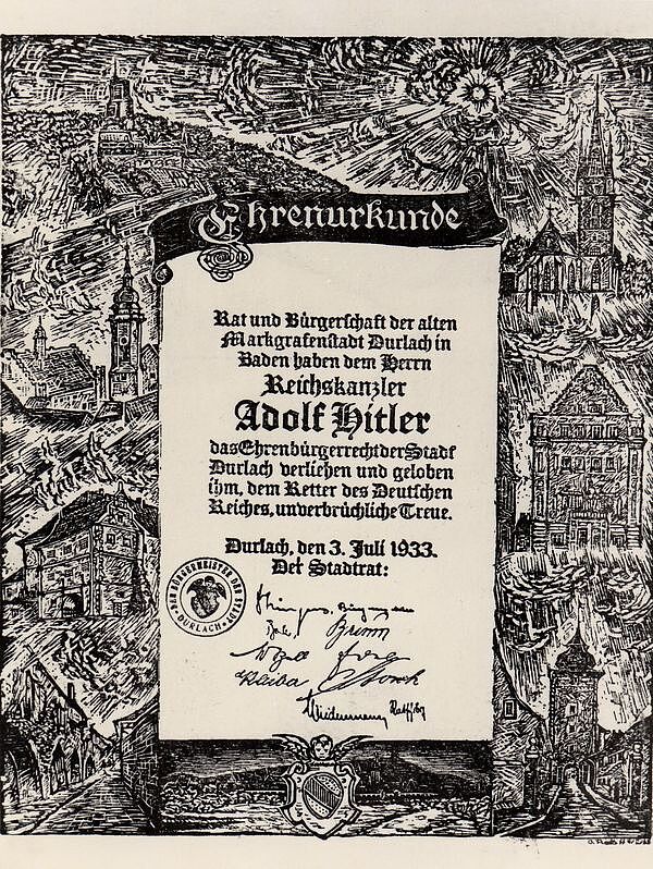 Ehrenurkunde der Stadt Durlach über das Ehrenbürgerrecht für Adolf Hitler. Eingerahmt durch schwarz-weiße Zeichnungen von Gebäuden der Text: Ehrenurkunde. Rat und Bürgerschaft der alten Markgrafenstadt Durlach in Baden haben dem Herrn Reichskanzler Adolf Hitler das Ehrenbürgerrecht der Stadt Durlach verliehen und geloben ihm, dem Retter des Deutschen Reiches, unverbrüchliche Treue. Durlach, den 3. Juli 1933. Der Stadtrat. Darunter mittig Unterschriften, links gestempelt das Siegel der Stadt Durlach.