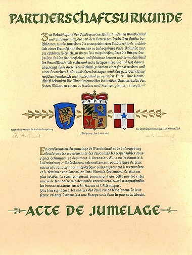Zu sehen ist eine zweisprachige Urkunde. Ober steht groß und grün Partnerschaft. Unter dem Text sieht man drei Wappen. Darunter kommt der französische Text, unter dem wiederum der französiche Titel groß in grün steht.